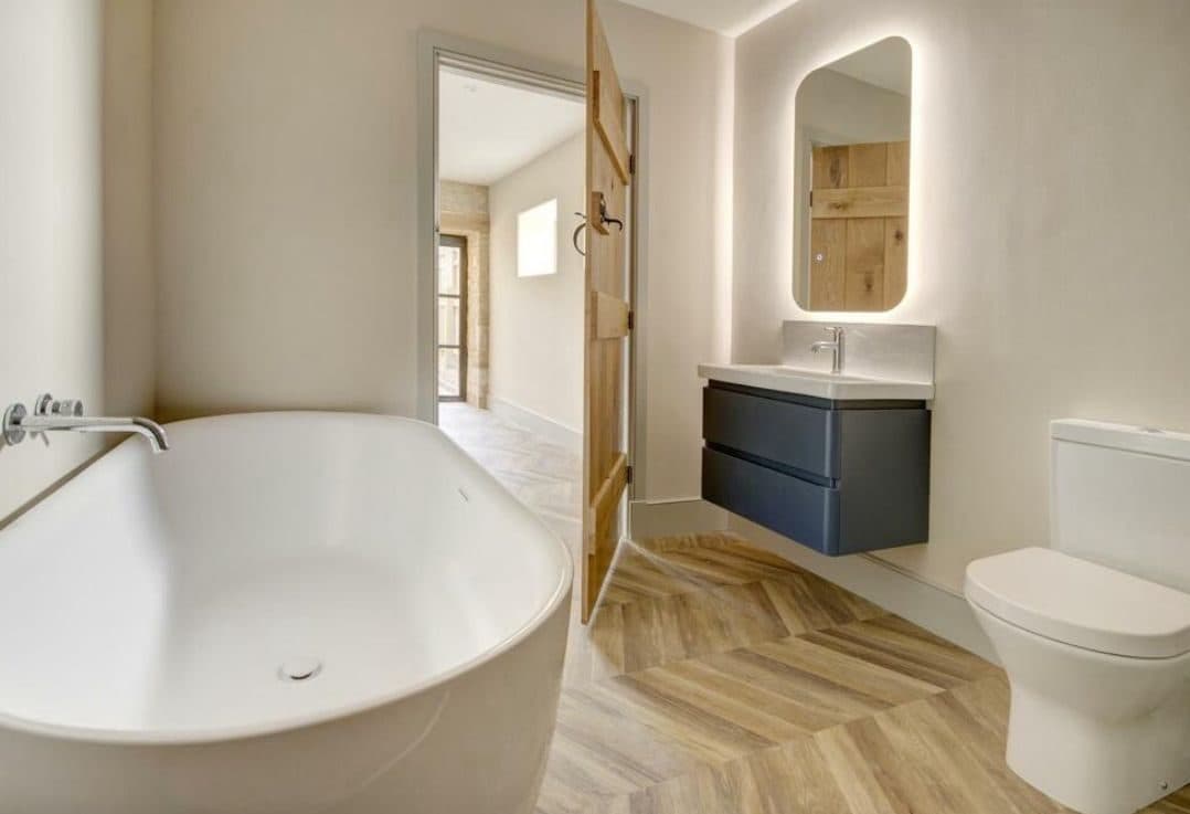 Bathroom with a freestanding bath, backlit mirror and herringbone floor