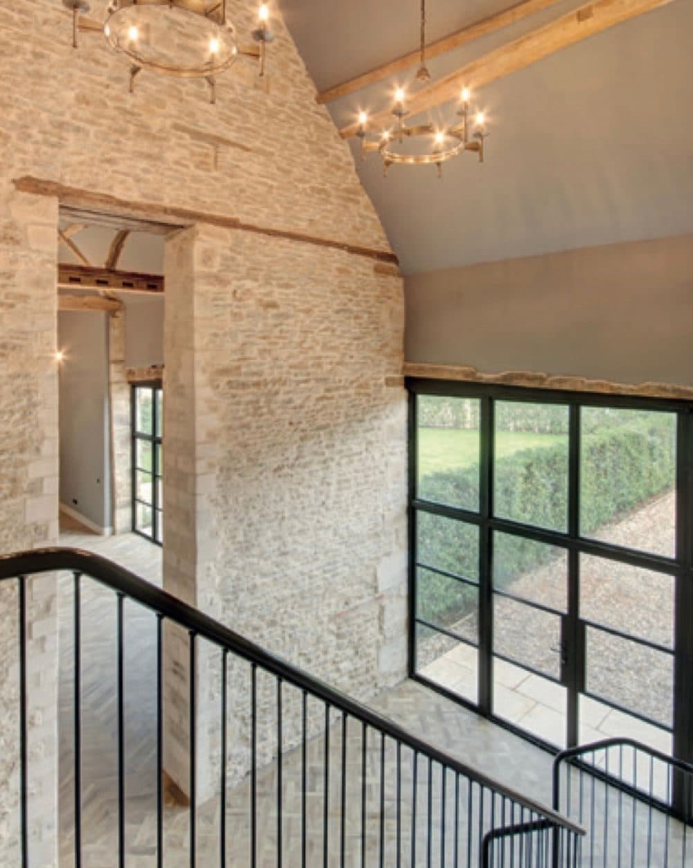Galleried barn landing with exposed stone, black steel windows and ring chandeliers