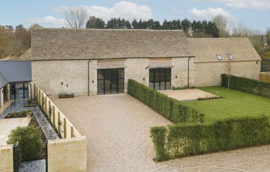 Exterior of a completed Cotswold stone barn conversion with black steel windows and gravel drive