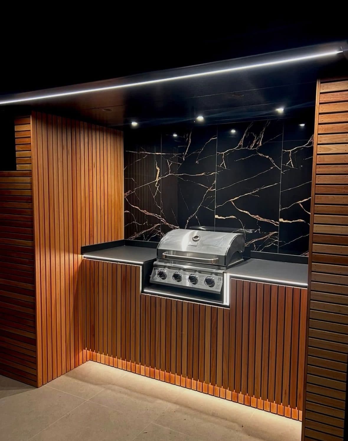 Outdoor kitchen with cedar slatted units, marble splashback and concealed strip lighting